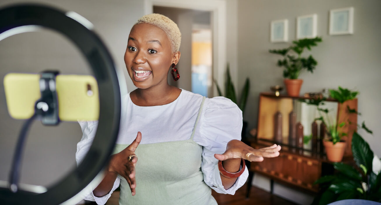 A Black woman stands in front of her phone making a video for social media, indicating that finding better money habits starts with finding good role models.